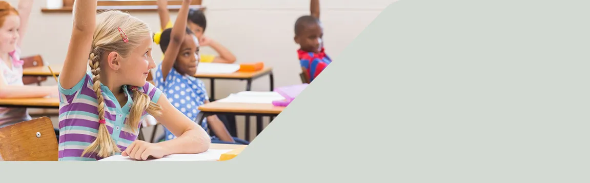 Grundschulkinder sitzen im Klassenzimmer an Tischen und melden sich