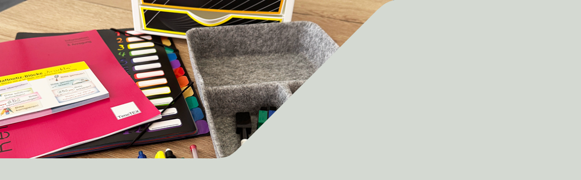 Auf einem Tisch liegen Planer, eine Fächermappe, Haftnotizen und eine graue Organisator-Box aus Filz mit Stiften und Stempeln
