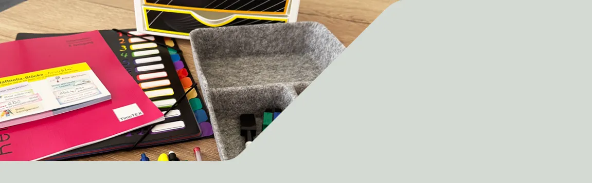 Auf einem Tisch liegen Planer, eine Fächermappe, Haftnotizen und eine graue Organisator-Box aus Filz mit Stiften und Stempeln